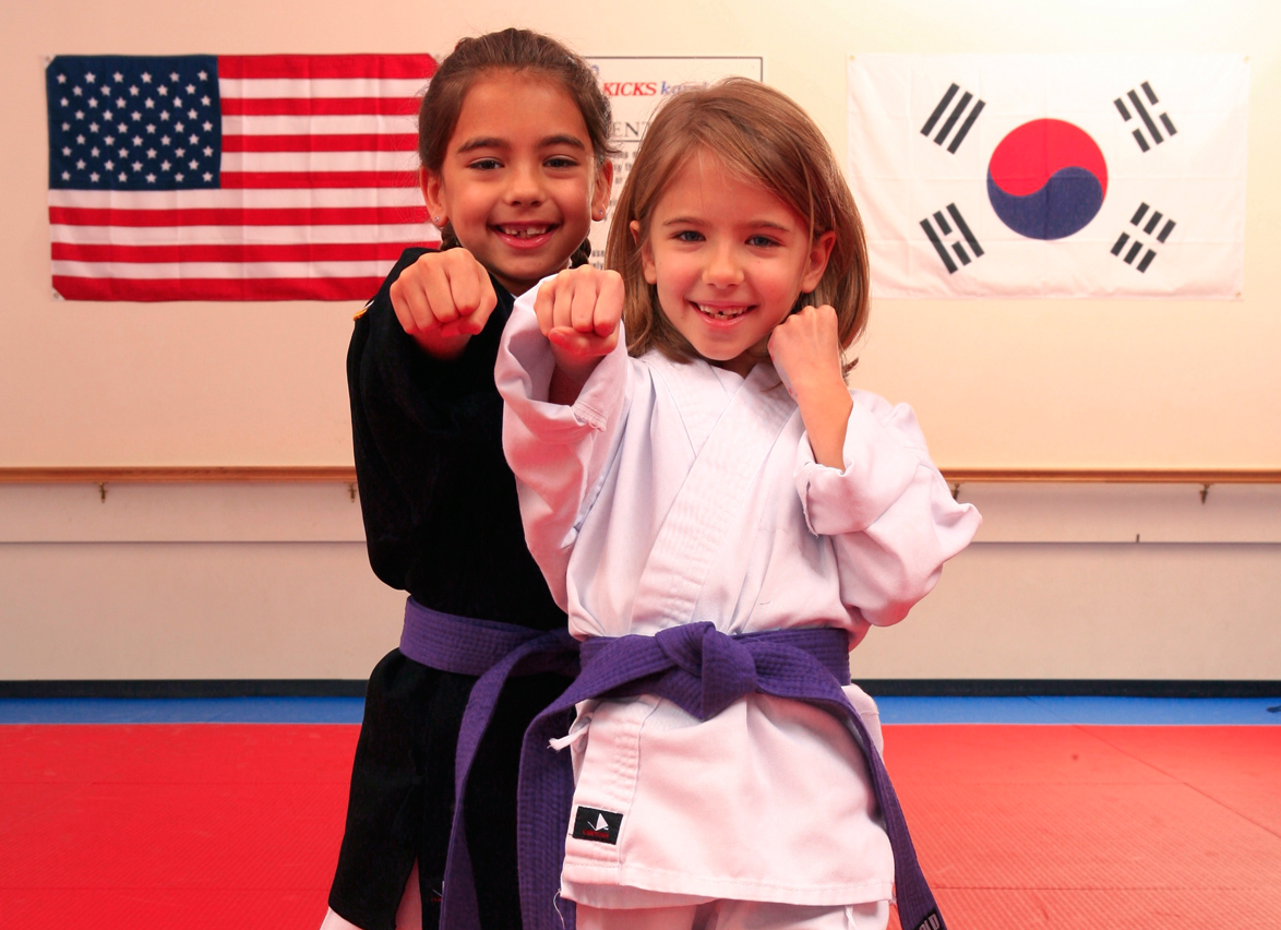 Two young children in karate uniforms with purple belts, smiling and ready to train